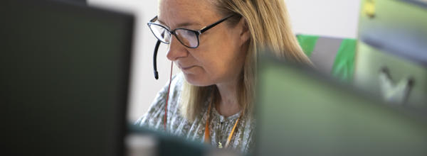 A woman is wearing a headset and looking at a computer screen.