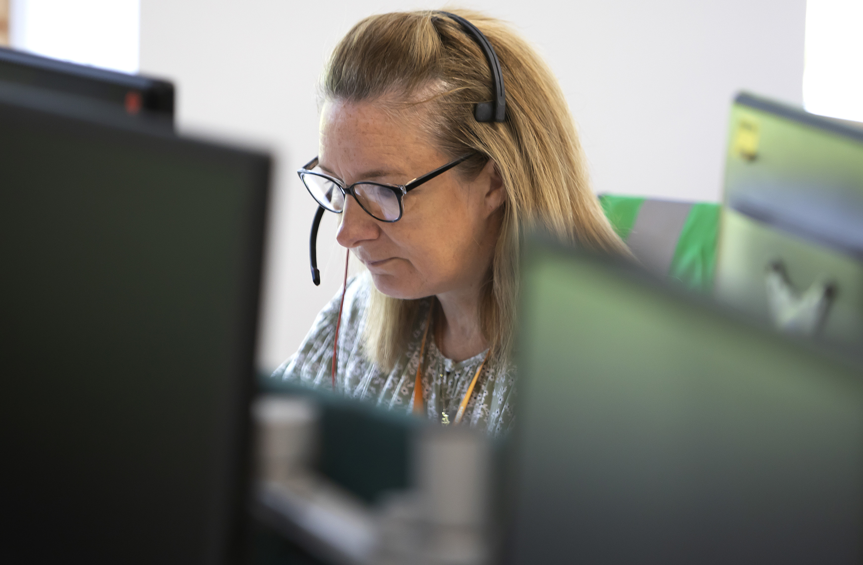 A woman is wearing a headset and looking at a computer screen.