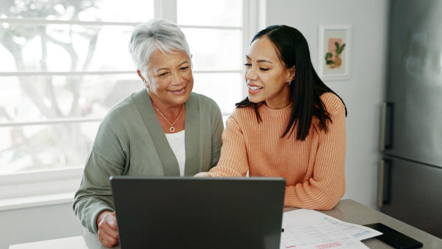 A younger woman is helping an older woman with her finances on a laptop.