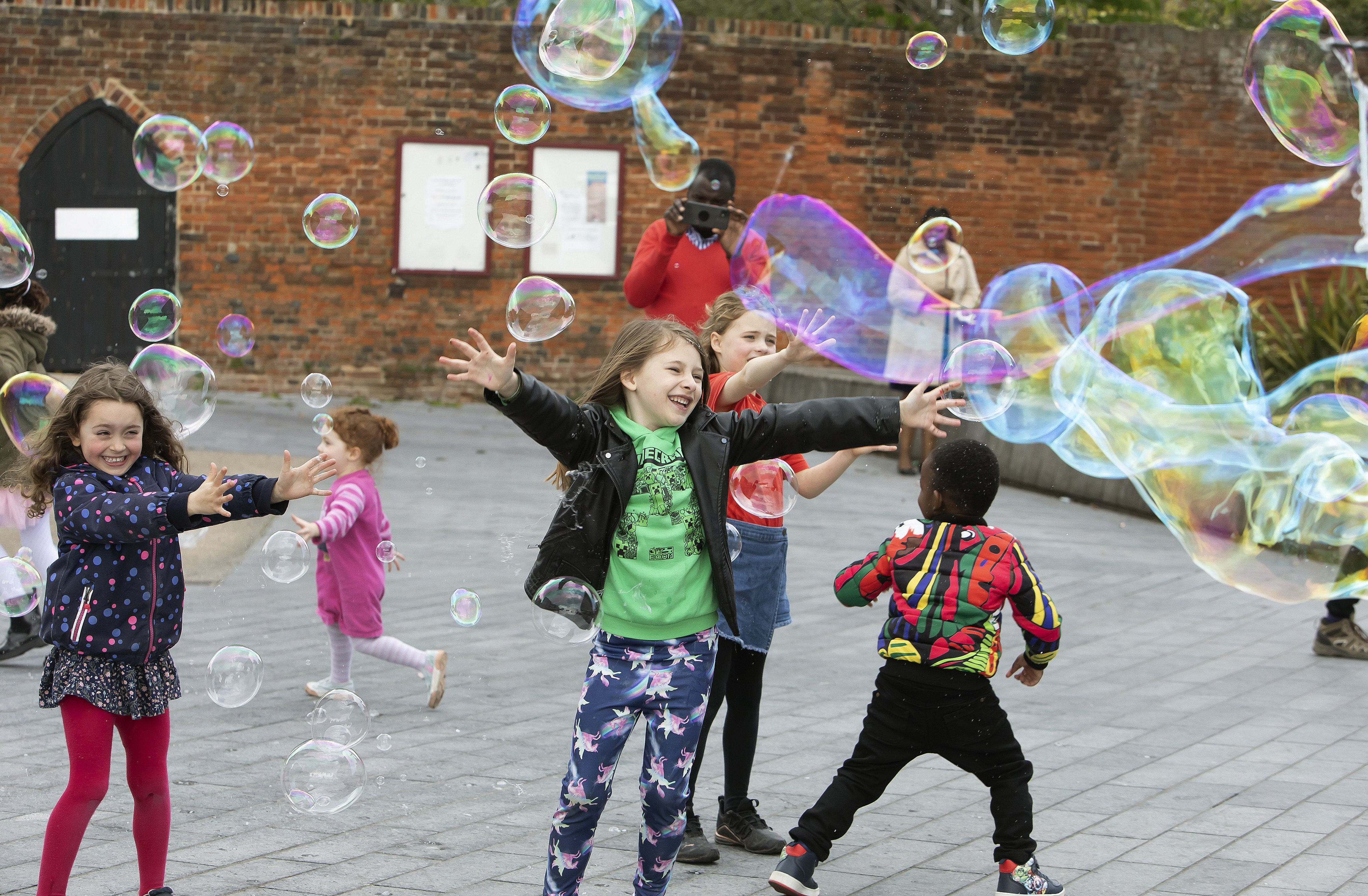 A group of children are playing with large bubbles outside an arts centre.