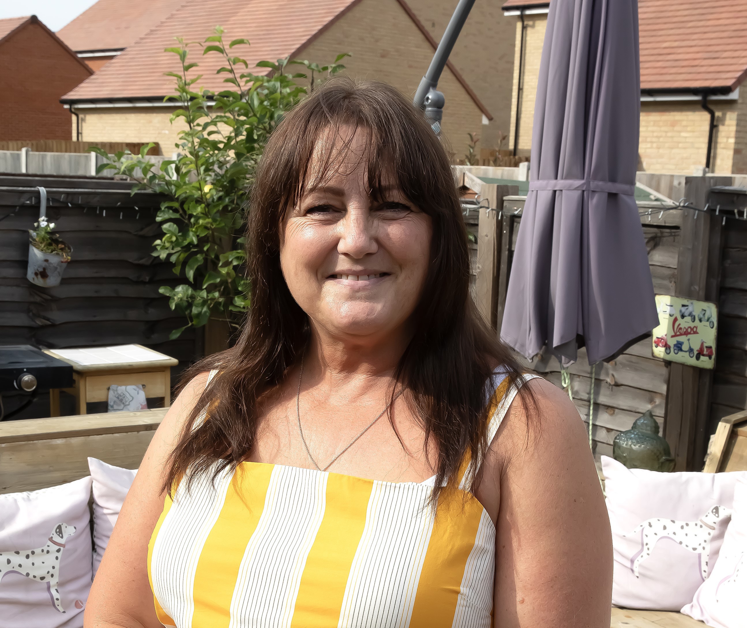 A woman in a yellow and white stripe dress is stood facing the camera and smiling.