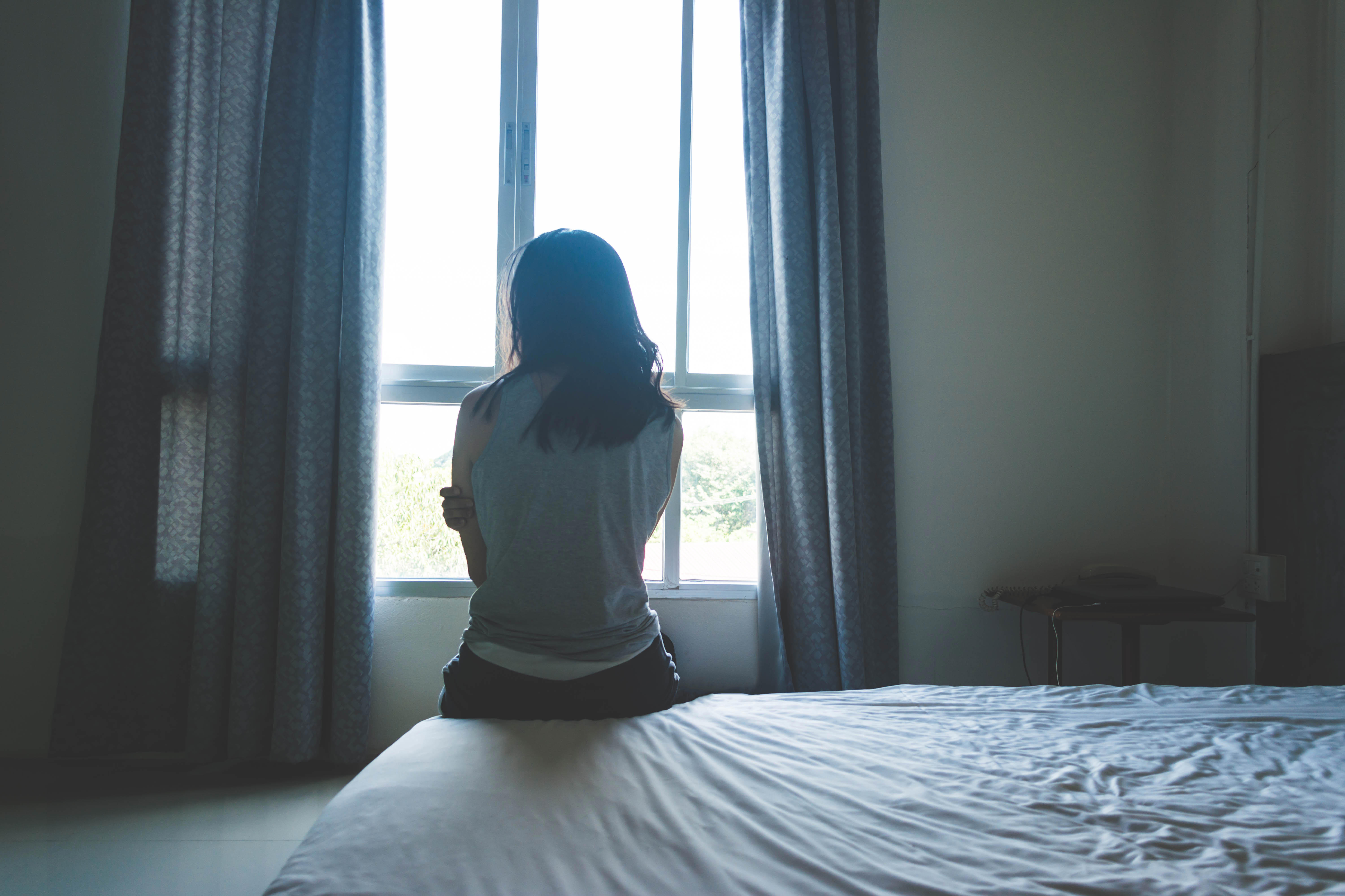 woman sitting on bed in room with light from window