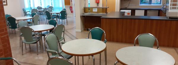 A room in Foundry Court with various tables and chairs around the tables. There is also a kitchen space to the right.