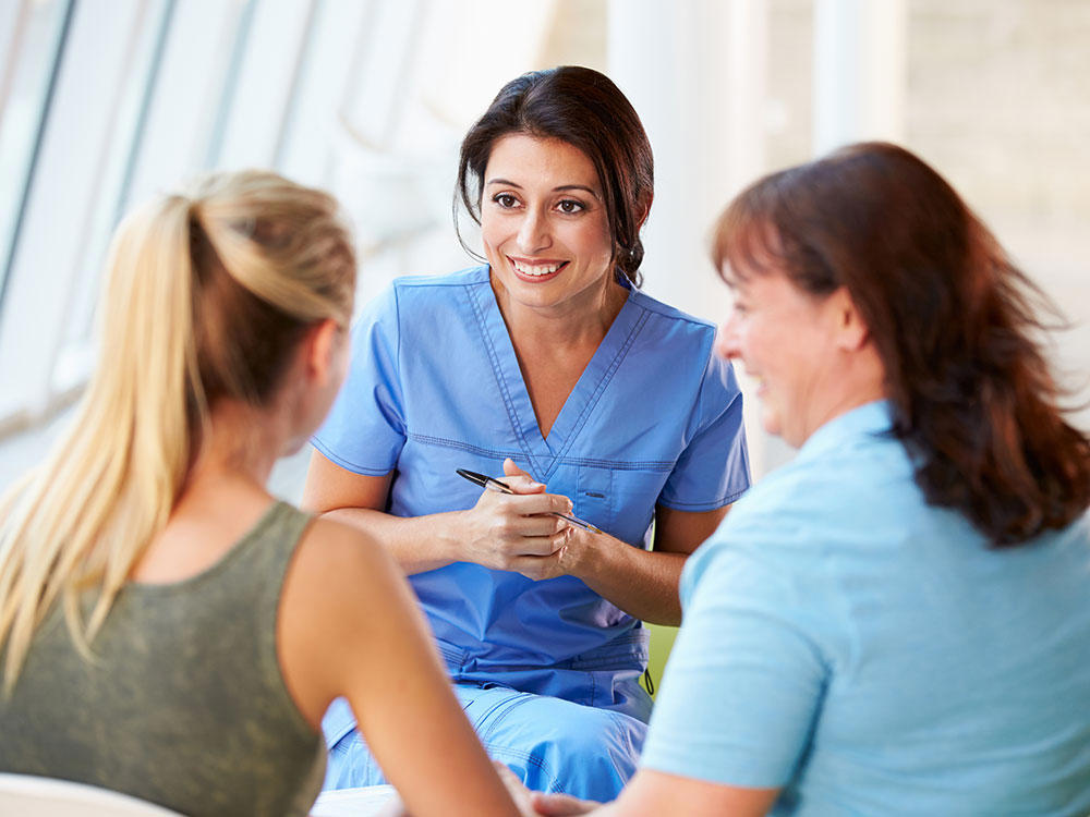 A woman in doctor's scrubs is talking to a young woman and an older woman.