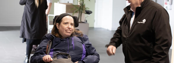 A woman in a wheelchair is speaking to a man stood next to her.