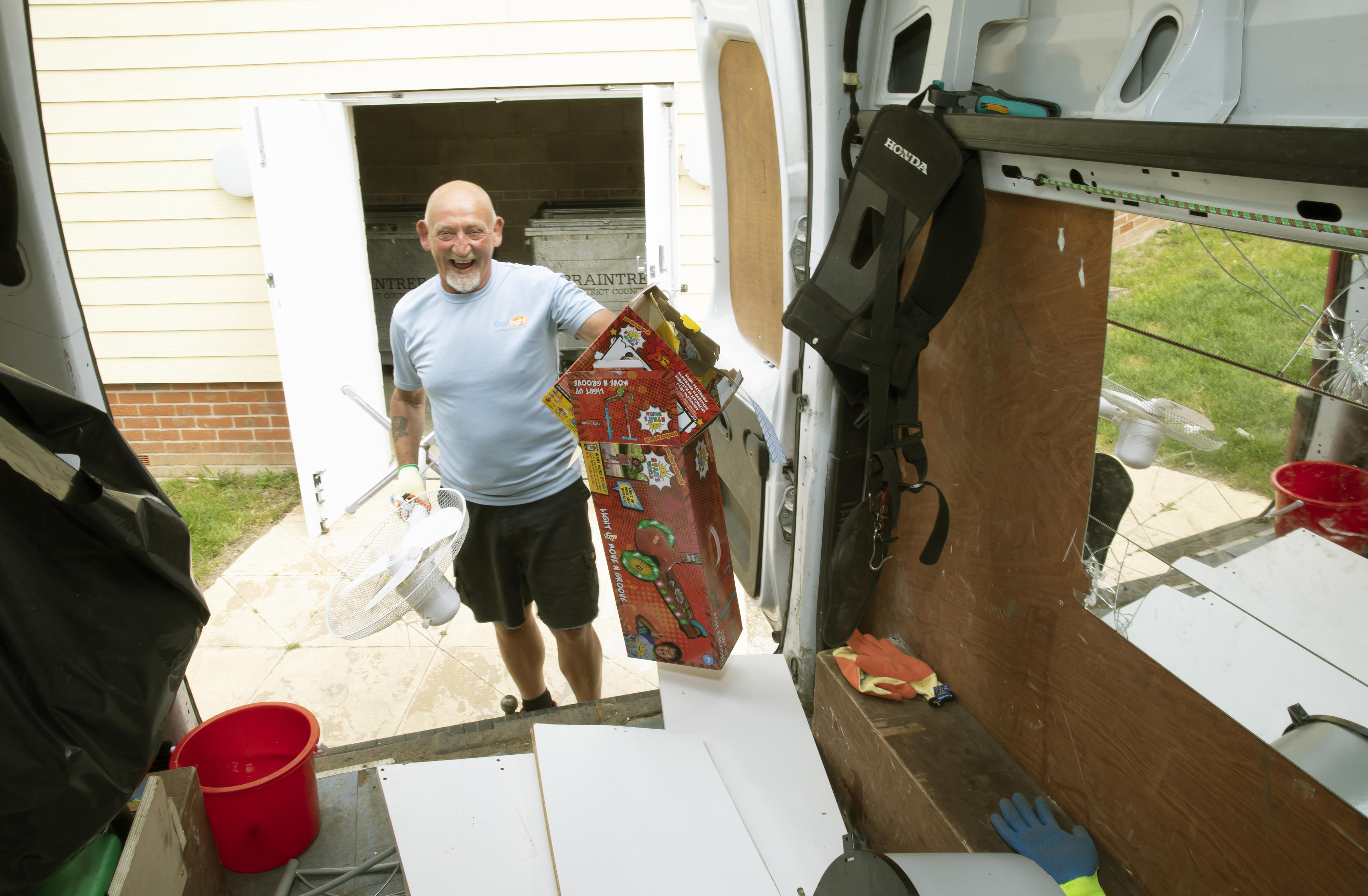 A man holding cardboard boxes and a fan. He is standing at the back of a van putting the items into the van.