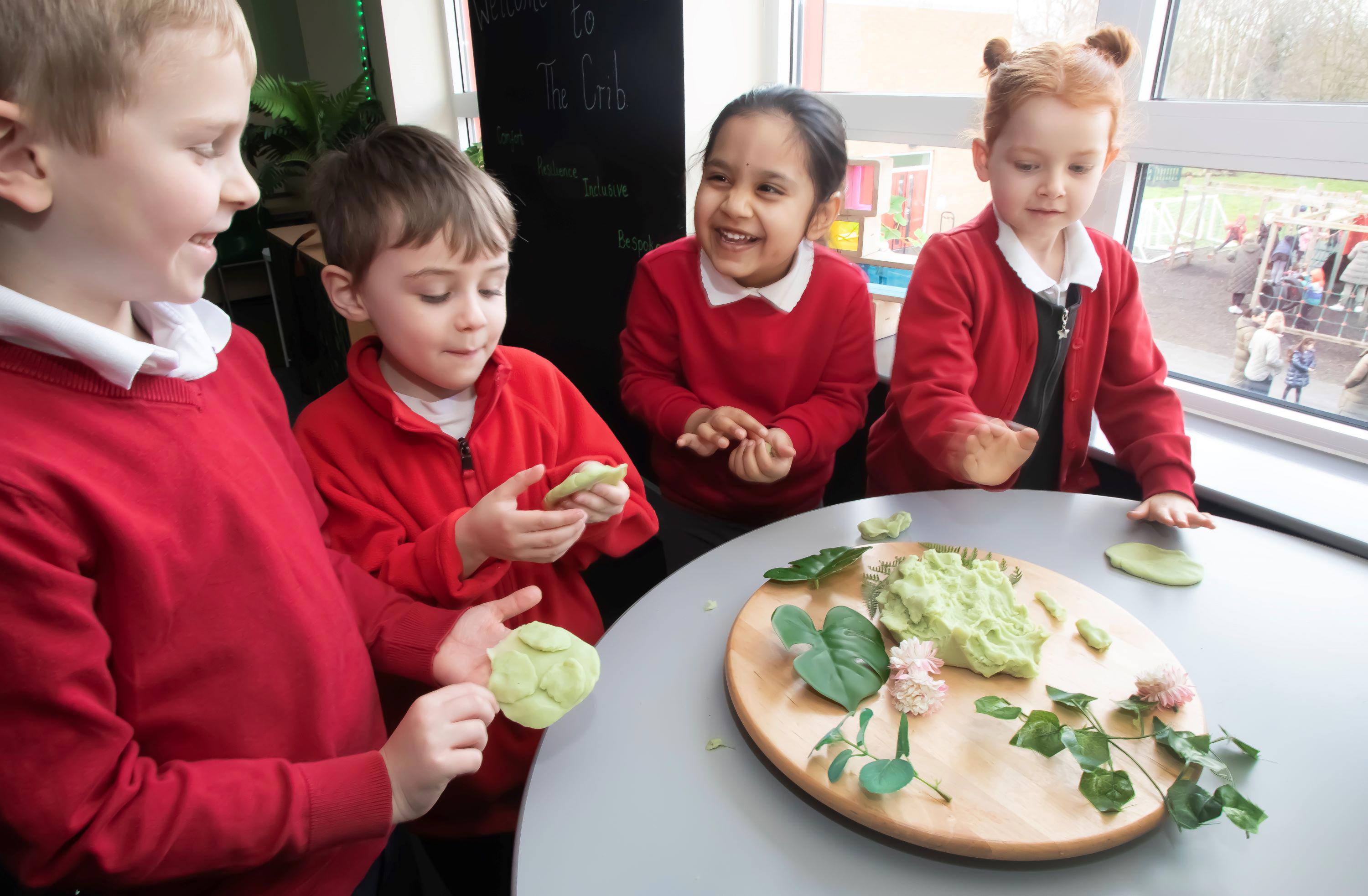 Young children wearing red jumpers are playing with slime.