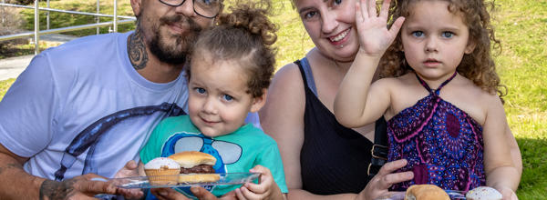 A man and woman are crouched down behind two young children. The family are all smiling at the camera.