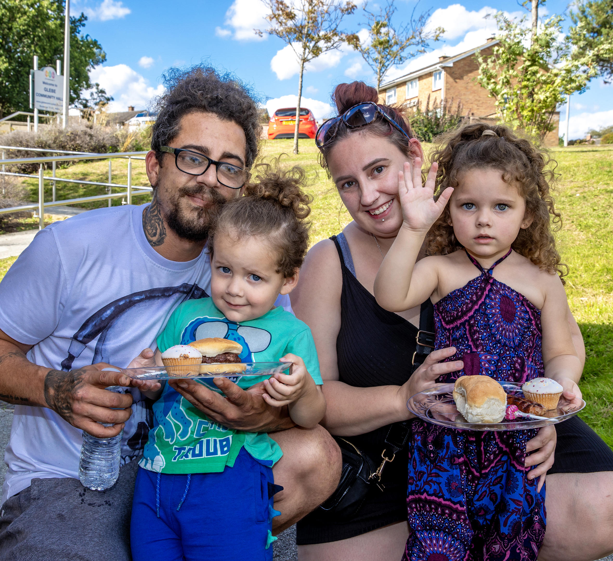 A man and woman are crouched down behind two young children. The family are all smiling at the camera.