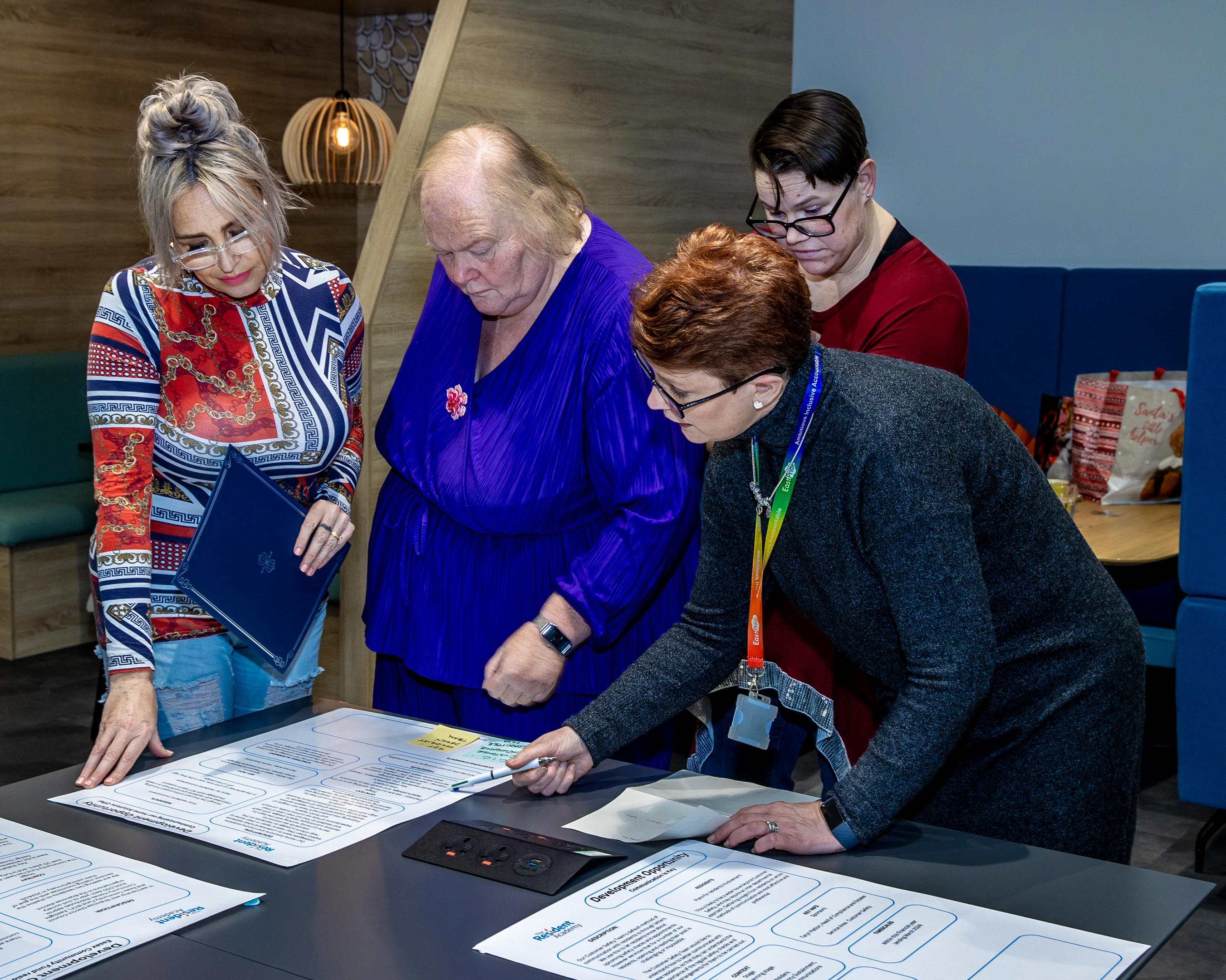 A group of four women are stood around a table looking at big pieces of paper which have been written on.