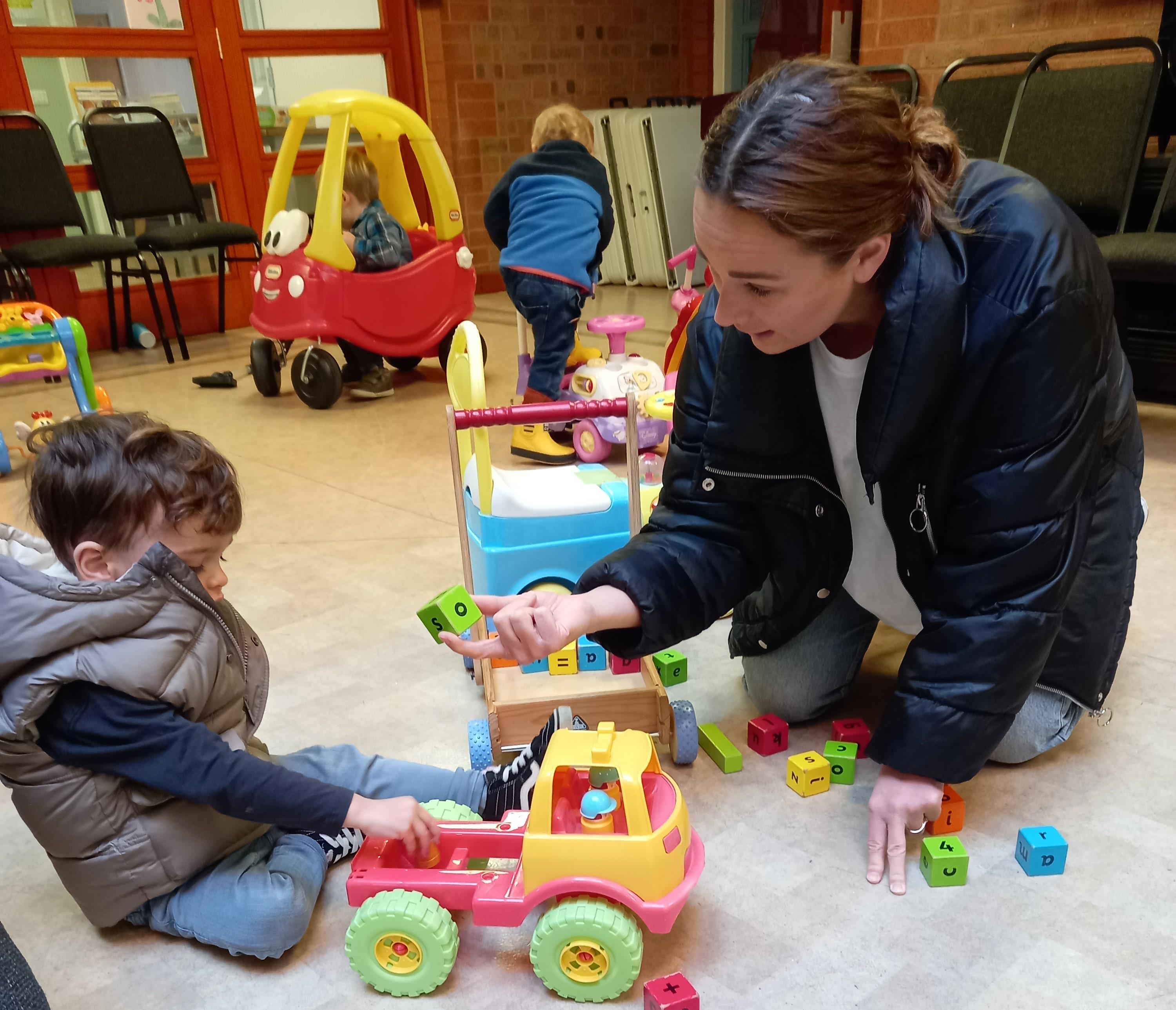 A woman and young boy are playing with toys on the floor.